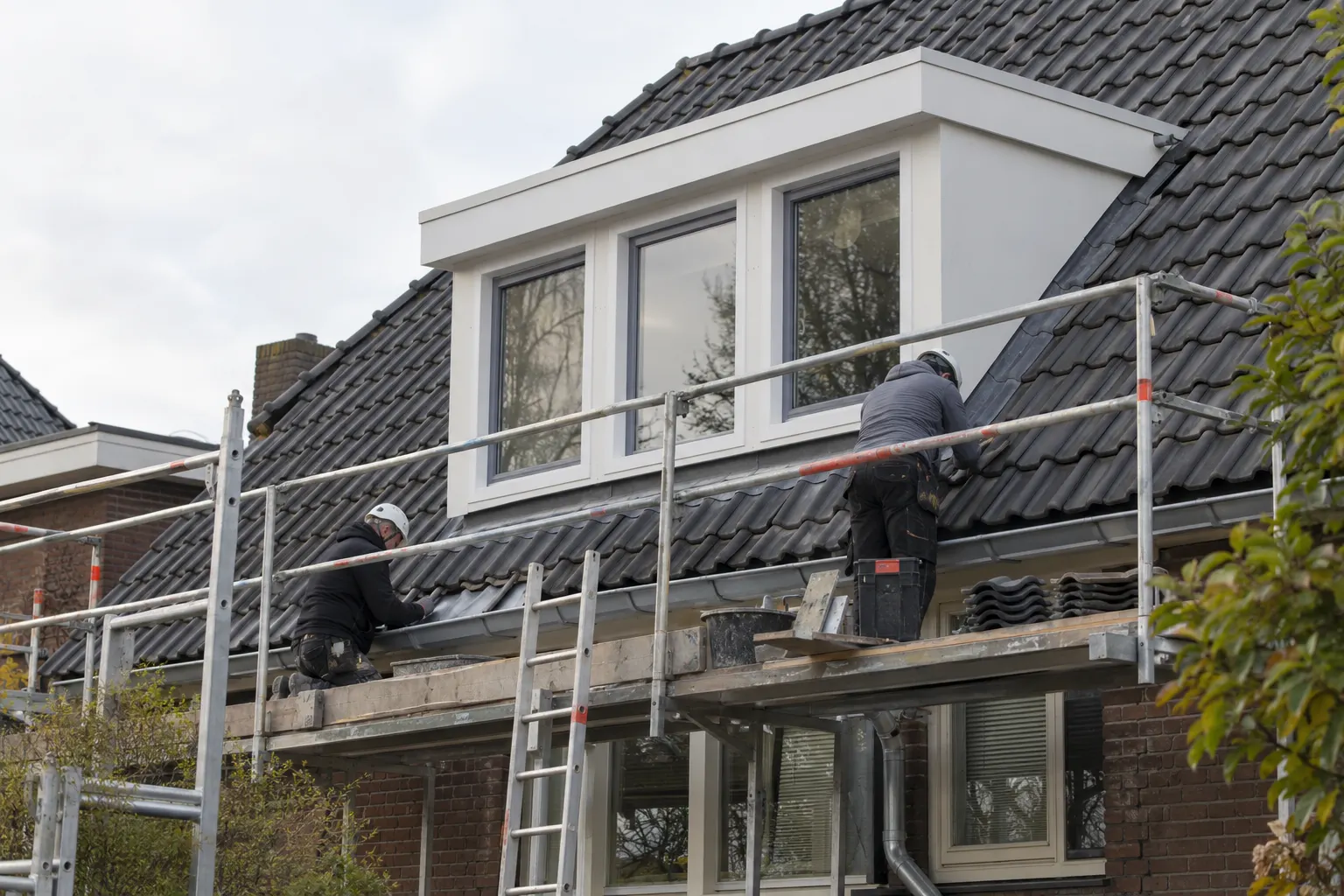 Witte dakkapel met donkere kozijnen die vanaf de steiger wordt afgewerkt