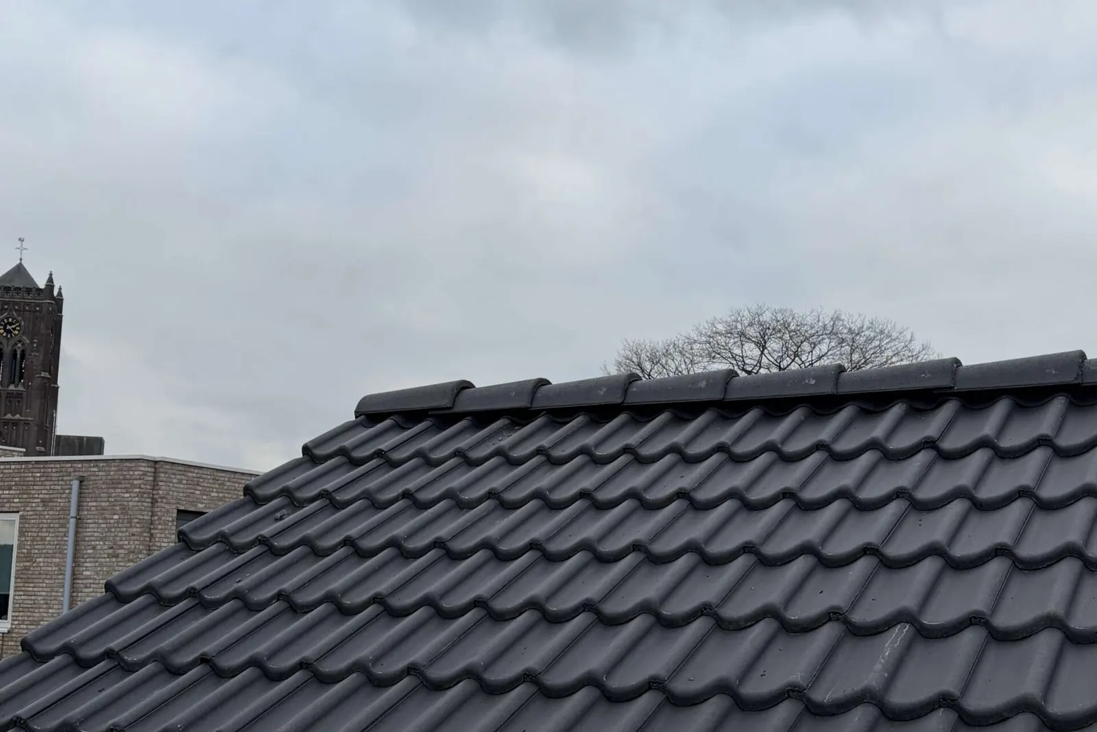 Nieuwe antraciet dakpannen met nokvorsten op een gerenoveerd dak