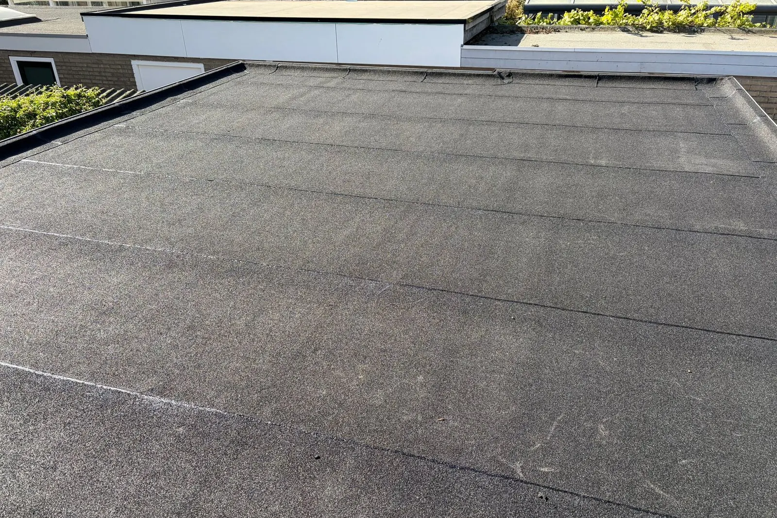 Nieuw bitumen plat dak met dakranden en doorvoeren strak afgewerkt